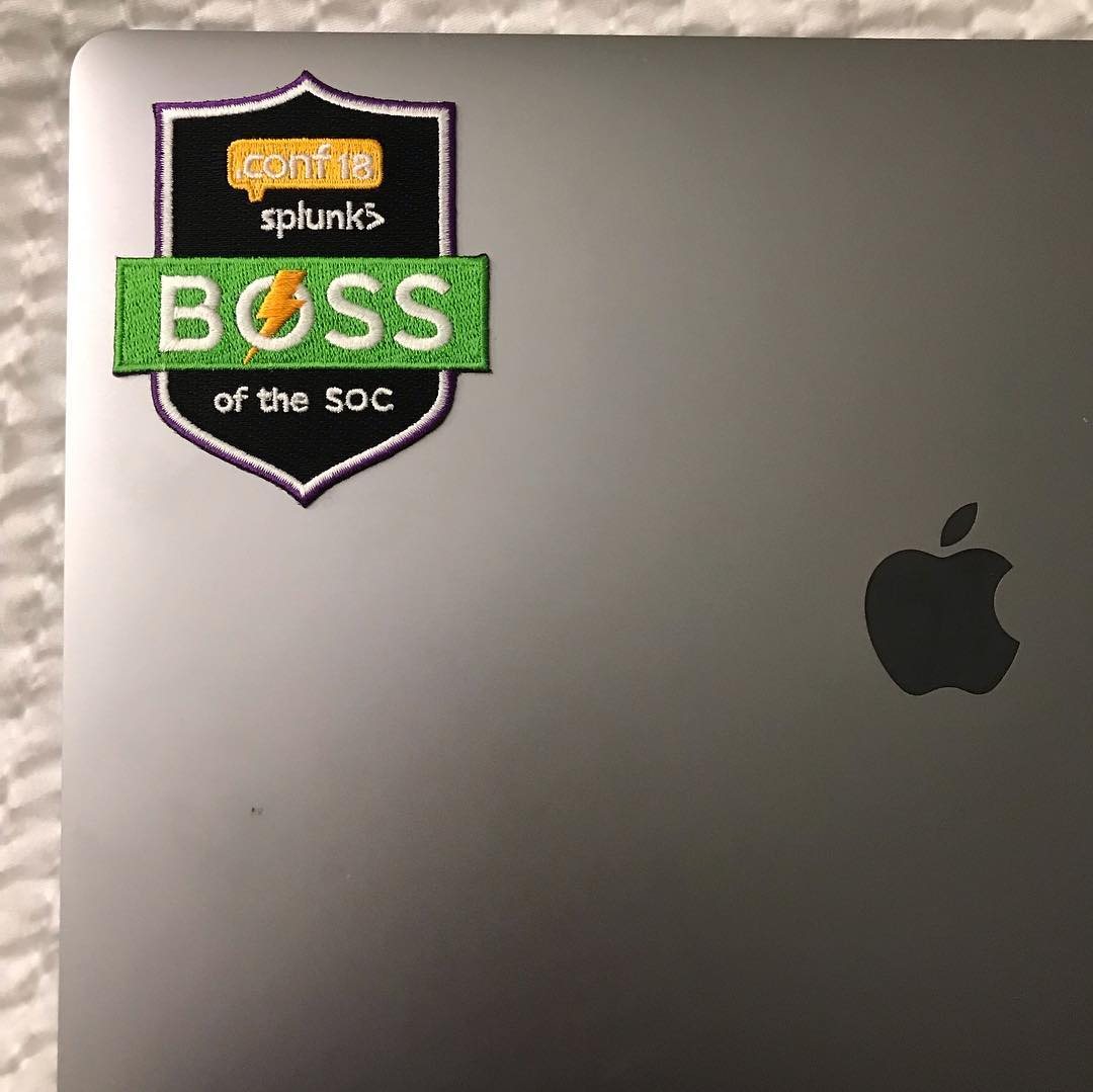 A woven .conf18 Boss of the SOC shield patch on a silver laptop lid.